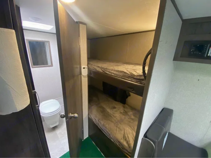 This RV rental interior shows a compact bathroom with a toilet, adjacent to cozy bunk beds, ideal for family travel.. Jayco Jay Flight SLX Baja Edition 2020