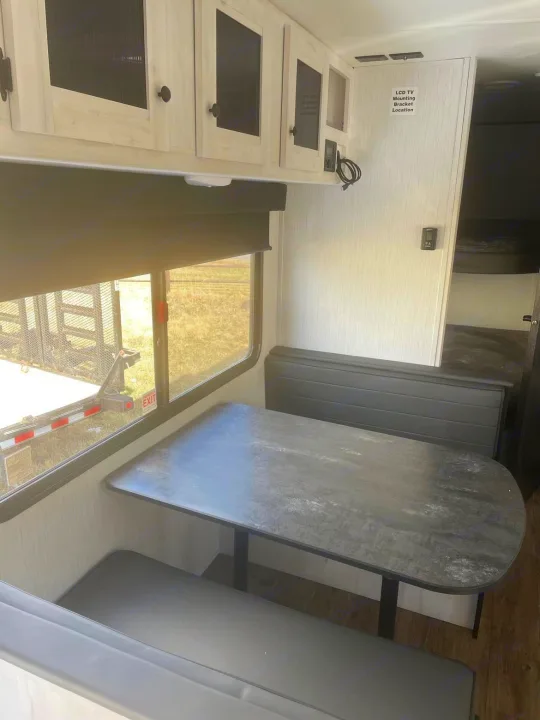 RV rental interior: A bright dinette with overhead cabinets, dark table & benches, and a window. Leads to bunk room.. Heartland RVs Trail Runner 2022