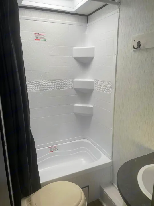 RV rental bathroom: white shower/tub, black curtain, toilet, and sink. Clean and compact.. Heartland RVs Trail Runner 2022