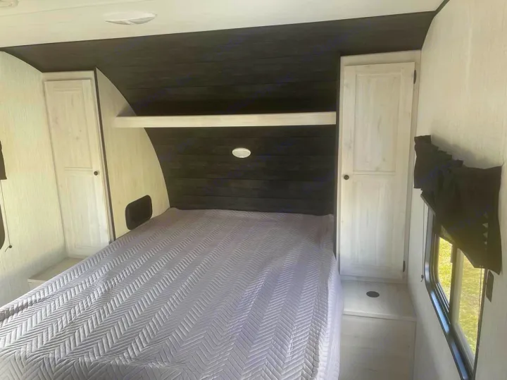 Cozy RV rental bedroom with a comfy bed, dark wood accents, and built-in storage. Perfect for travel!. Heartland RVs Trail Runner 2022