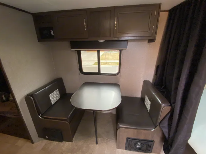 Cozy RV rental interior features a dinette with dark benches, table, and overhead cabinets.. Jayco Jay Flight SLX Baja Edition 2020