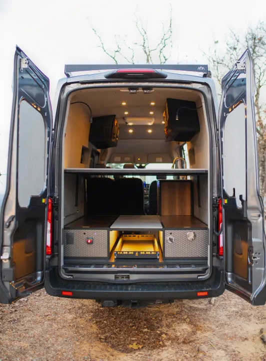 Inside a modern RV rental van conversion: organized storage, task lighting, and a pull-out kitchen/gear tray for travel.. Ford Transit 2021