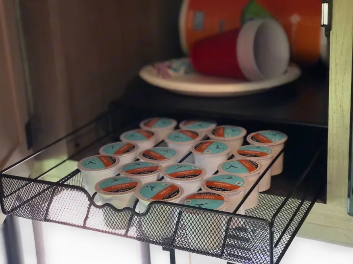 RV rental kitchen: Organized Caribou Blend K-cups in a pull-out drawer, with cups and plates in the background.. Forest River Coachmen Cross Trail XL 2022
