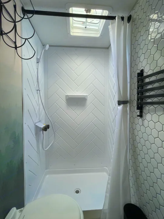 Modern RV rental bathroom features a compact shower with herringbone walls, hex tiles, and a skylight.. Forest River 178BHSKX 2022