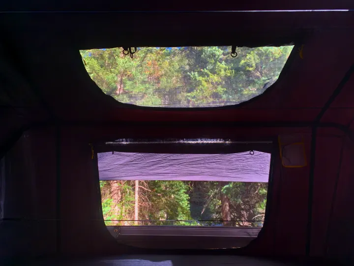 Serene nature view from an RV rental's rooftop tent, showing trees through mesh windows and a partial blind.. Smittybilt Overlander XL Gen 2 RTT 2021
