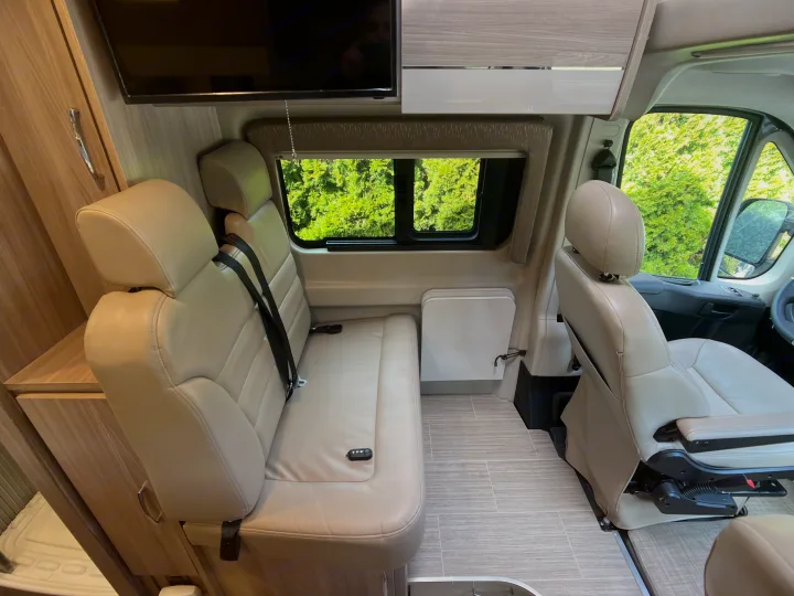 Spacious RV rental interior with light-colored seating, wall-mounted TV, and flexible living area.. Dodge Ram Thor Thor 2022