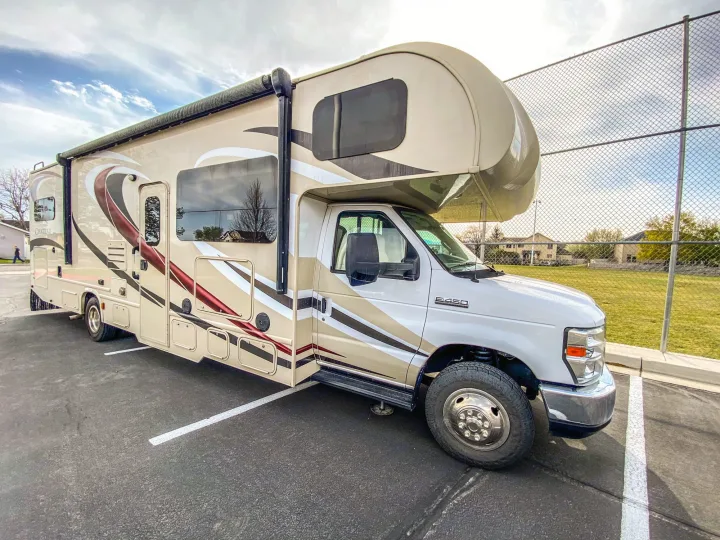 This beige Chateau Class C rv rental is parked on asphalt, awaiting its next adventure under a partly cloudy sky.. Thor Chateau 2016