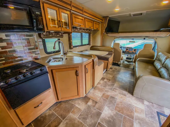 Enjoy this RV rental interior featuring a full kitchen with microwave, stove, sink, dining booth, and sofa.. Thor Chateau 2016