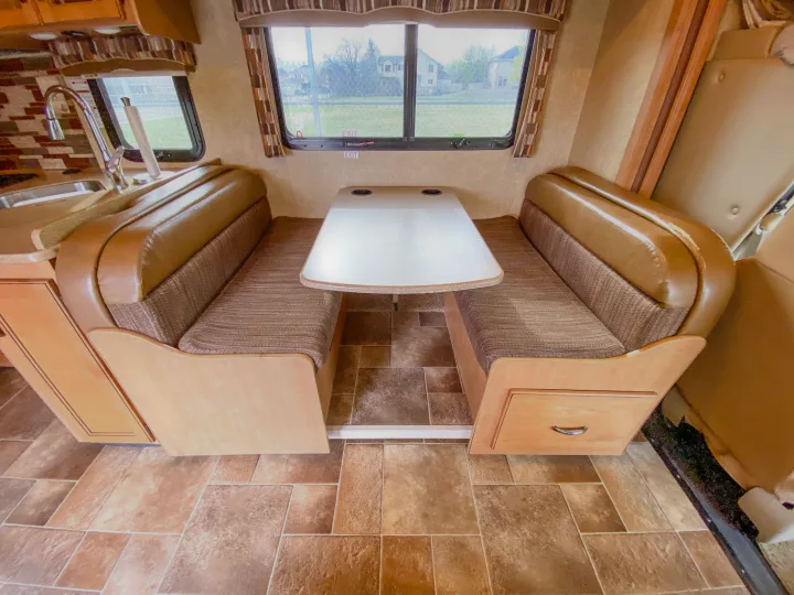 RV rental interior shows a cozy dinette with tan benches, a white table, and a kitchen counter with a sink.. Thor Chateau 2016