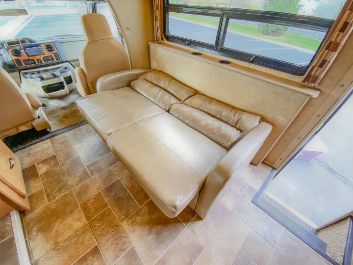 Interior of an RV rental showing a plush leather sofa, tiled floor, and the driver's area with dashboard.. Thor Chateau 2016