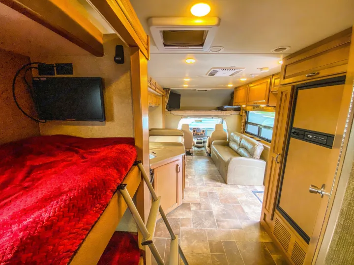 Full view of a spacious RV rental interior: bunk beds, kitchen, living area with sofa, and front cab.. Thor Chateau 2016