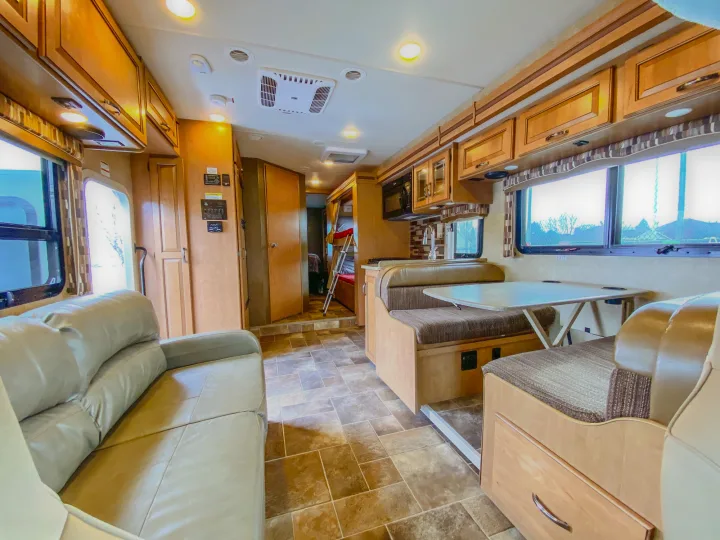Bright RV rental interior features a spacious living area with sofa, dining booth, and rear bunk beds.. Thor Chateau 2016