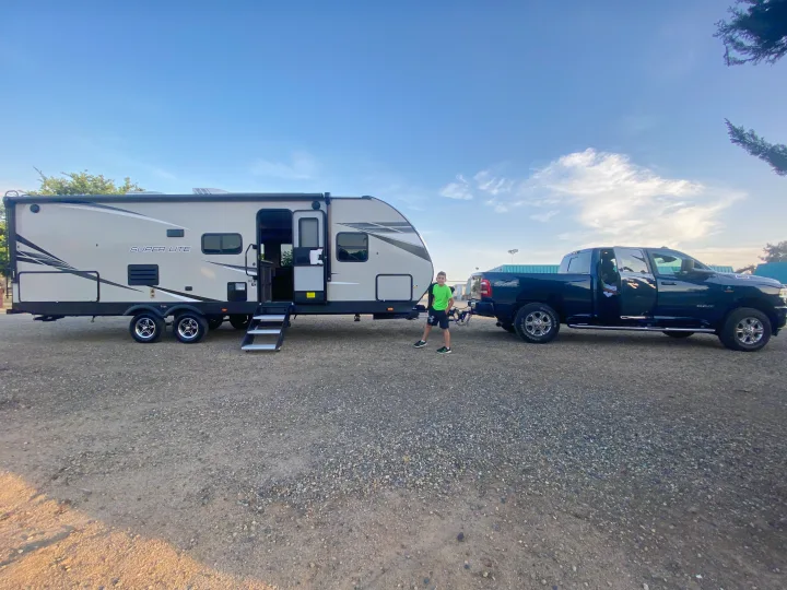 Ready for adventure with this RV rental! A young boy stands by a travel trailer hitched to a pickup truck under blue skies.. Starcraft Super Lite 2022