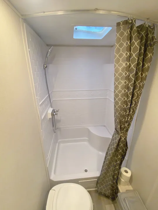Inside an RV rental: a compact bathroom featuring a full shower, toilet, and patterned curtain for comfortable travel.. Other Tracer 2022