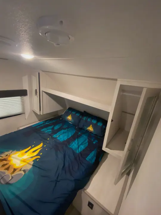 Inside an RV rental: a cozy bedroom with campfire bedding, built-in storage, and a window. Compact for comfortable travel.. Other Tracer 2022