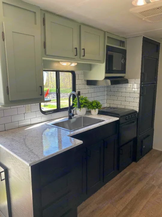 Experience comfort in this renovated RV rental kitchen, featuring sage green/black cabinets, white backsplash, and modern appliances.. Gulf Stream Conquest 2015