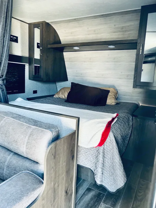 Modern rv rental interior: a clean bedroom with light wood walls, dark cabinets, and a comfortable bed with a white blanket.. Jayco Jay Flight SLX Rocky Mountain Edition 2021
