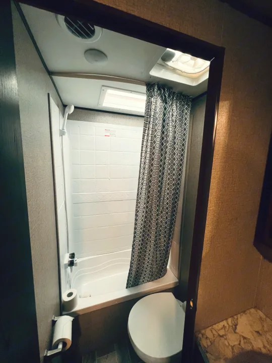 View inside an RV rental bathroom: compact shower/tub with patterned curtain, toilet, and overhead skylight.. Jayco Jay Flight SLX Rocky Mountain Edition 2021