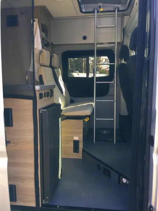 Inside an RV rental: compact interior with light seats, wooden cabinetry, windows, and safety bars.. Winnebago Solis 2022