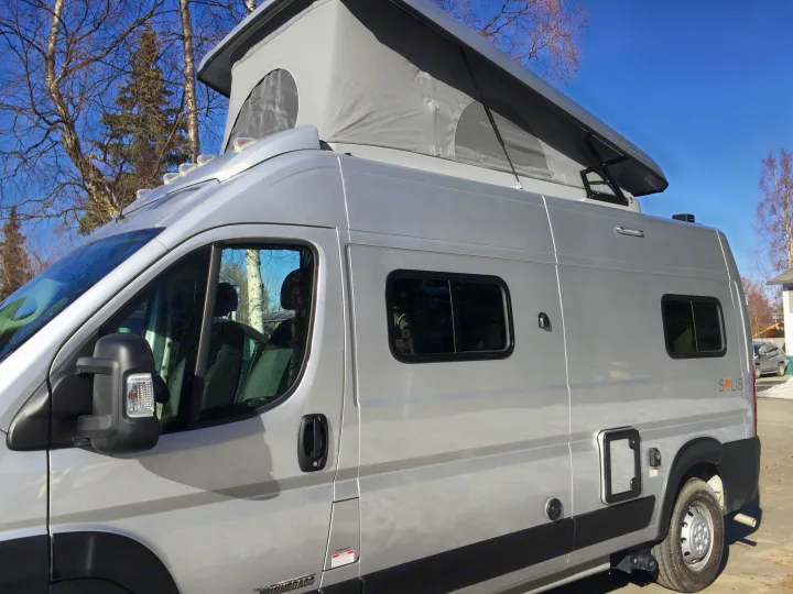 Grey Winnebago Solis **rv rental** with a pop-top roof extended, parked outdoors under a clear blue sky.. Winnebago Solis 2022