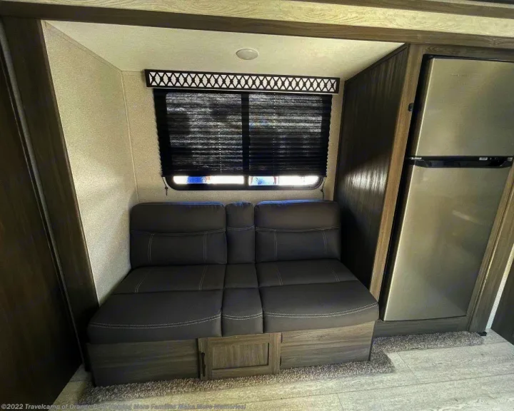 This RV rental offers a compact interior with a grey sofa, window with blinds, and a stainless steel refrigerator.. Shasta 25RS 2021