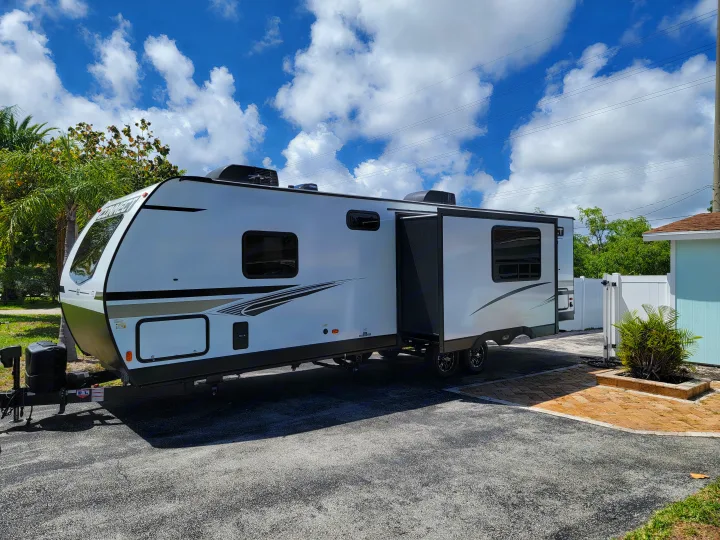 White travel trailer RV with slide-out extended, parked on asphalt under blue skies. Ideal for rv rental adventures!. Otherl Other 2022