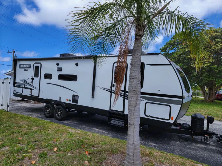 A white 'CONNECT KZ' travel trailer, ideal for your next RV rental, parked on asphalt beside a palm tree.. Otherl Other 2022