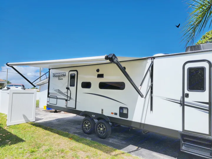 Bright sunny day showcasing a white travel trailer RV rental with its awning extended, parked on asphalt next to grass.. Otherl Other 2022