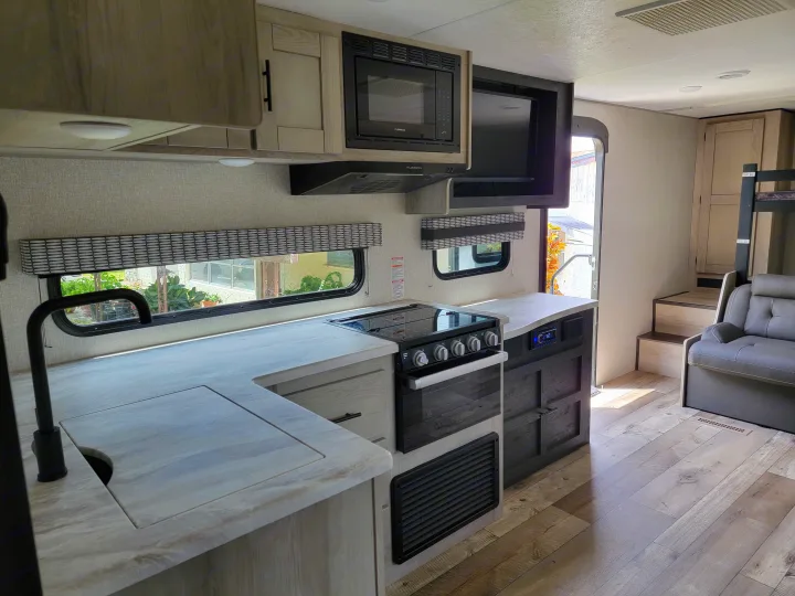 Spacious RV rental interior with a bright, modern kitchen (stove, microwave, sink), living area with sofa, and bunk beds.. Otherl Other 2022