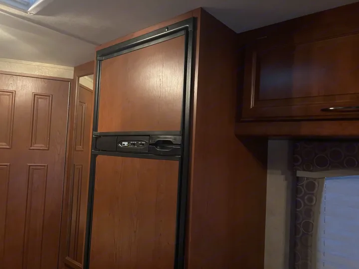 RV rental interior showcasing a wood-paneled refrigerator, adjacent cabinets, and doors, providing a cozy living space.. Thor Chateau 2012