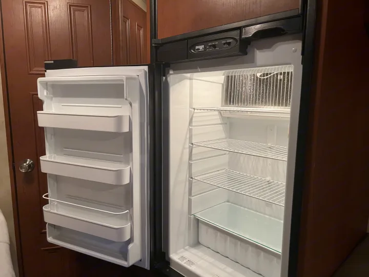Empty, clean RV rental refrigerator & freezer. The open interior shows white door bins, wire shelves, & bottom glass shelf.. Thor Chateau 2012