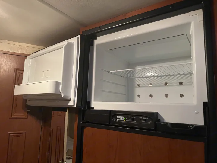 An open, empty compact refrigerator and freezer, likely in an RV rental. Norcold controls are visible.. Thor Chateau 2012