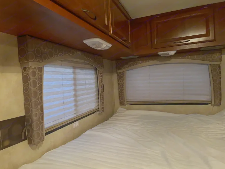 Cozy RV rental bedroom featuring a comfortable bed, windows with blinds, and convenient overhead storage.. Thor Chateau 2012