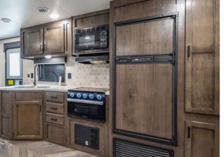RV rental kitchen: modern wood cabinets, fridge, microwave, stove, sink, and hexagonal backsplash.. Highland Ridge Olympia 26BHS 2022