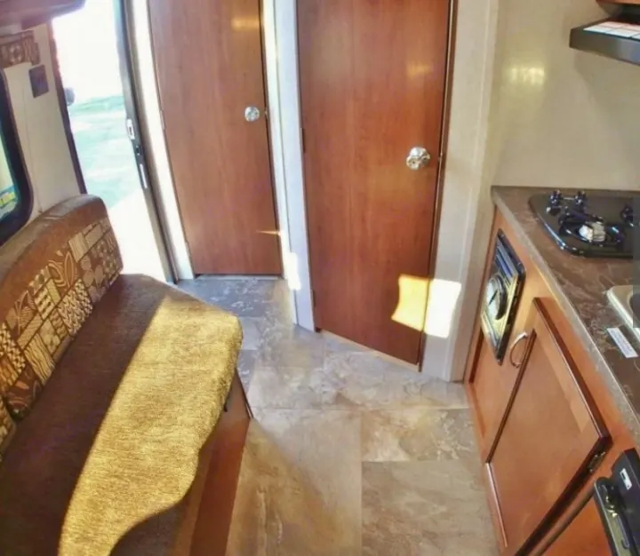 RV rental interior: kitchen with stove/sink, cozy dinette, and two wood-paneled doors. Bright, compact travel space.. Jayco Jay Flight 2016