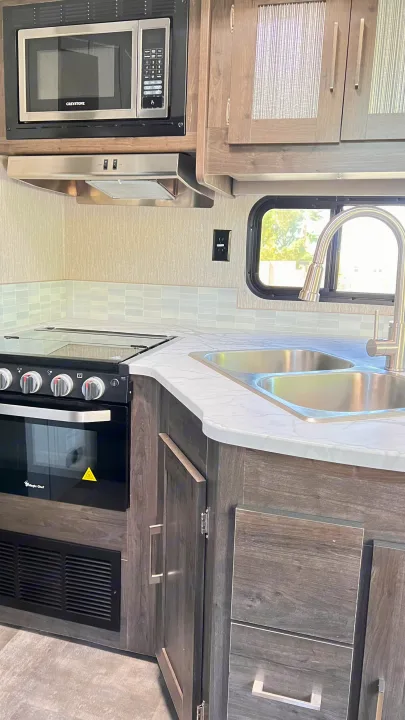 Modern RV rental kitchen with microwave, oven/stove, and dual sink. Stylish cabinetry and backsplash complete the galley.. Forest River Coachmen Pursuit 2022