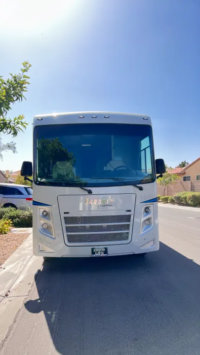 Front view of a white RV, likely an rv rental, parked on a sunny street. Features include its large windshield, grille, and headlights.. Forest River Coachmen Pursuit 2022