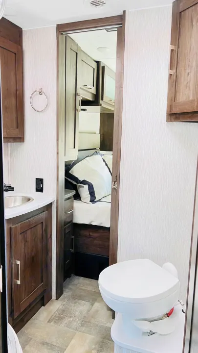 RV rental interior: A compact, modern bathroom with sink and toilet, leading to a cozy bedroom. Efficient design for travel.. Forest River Coachmen Pursuit 2022