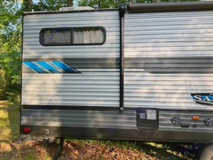 Side view of a light gray travel trailer with blue graphics, perfect for an RV rental adventure. Shows window, awning, and lower panel details.. Forest River Salem 2021