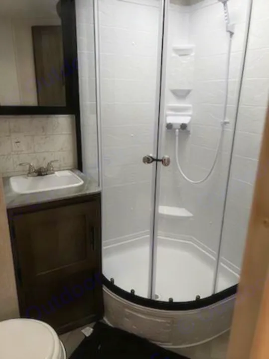 Bright RV rental bathroom with a modern corner glass shower enclosure, a white basin sink, and dark wood vanity.. Forest River Salem 2021