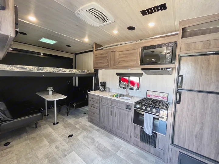 Modern RV rental interior: kitchen with stove, fridge, and sink; dining area with bunk bed overhead.. Pacific Coachworks Blaze'N 2022