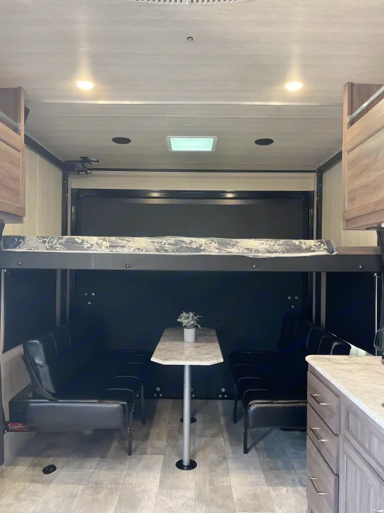 RV rental interior: versatile space with a dining table, seating, pull-down bunk bed, and wood flooring.. Pacific Coachworks Blaze'N 2022