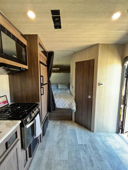 RV rental interior: kitchen with microwave/stove, fridge, and bed with privacy curtain. Compact yet well-equipped for travel.. Pacific Coachworks Blaze'N 2022