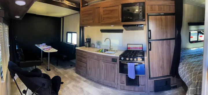 Spacious RV rental interior featuring a modern kitchen with stove/fridge, dining table, and comfy bedroom area.. Pacific Coachworks Blaze'N 2022