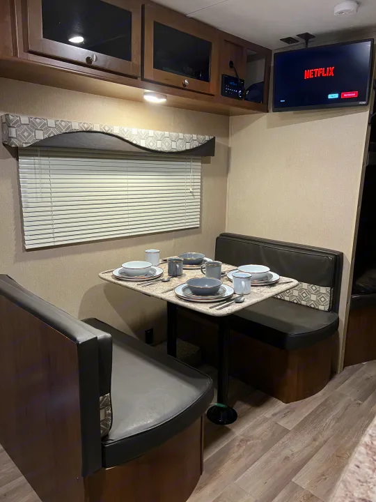 Inside an RV rental: A well-appointed dining booth with a set table, overhead cabinets, and a TV tuned to Netflix.. Aspen Trail Aspen Trail Trailer 2018