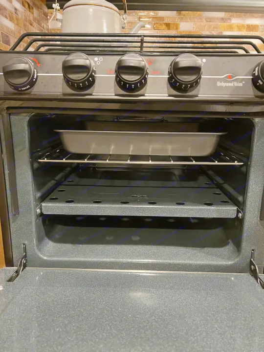 RV rental kitchen: Open oven with a baking pan on a rack. Stove top has controls for burners & oven. Wedgewood Vision model.. Aspen Trail Aspen Trail Trailer 2018