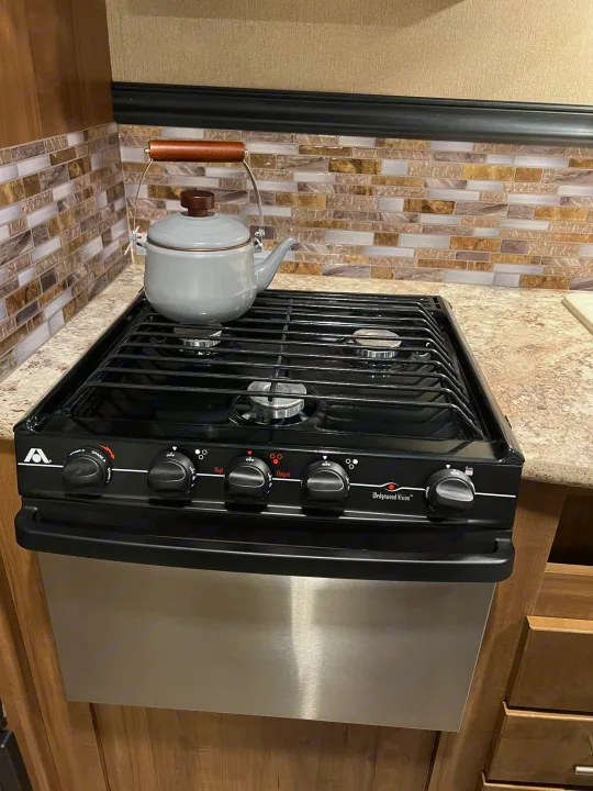 RV rental kitchen with a gray teapot on a gas stovetop, featuring a stainless steel oven and tile backsplash.. Aspen Trail Aspen Trail Trailer 2018