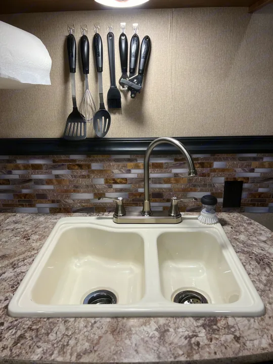 Functional RV rental kitchen: cream double sink, chrome faucet, tiled backsplash, and hanging utensils.. Aspen Trail Aspen Trail Trailer 2018