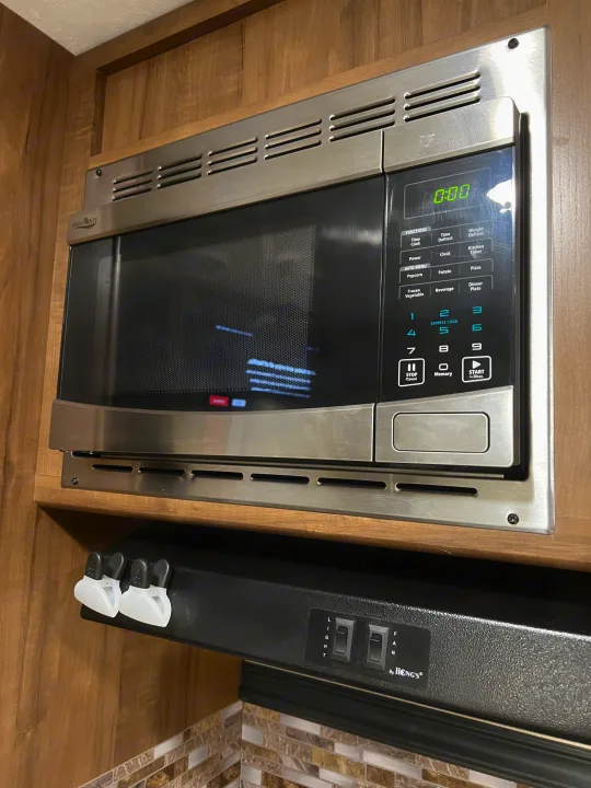 An rv rental kitchen with a stainless steel High Pointe microwave oven and a Hong's range hood with visible light and fan switches.. Aspen Trail Aspen Trail Trailer 2018