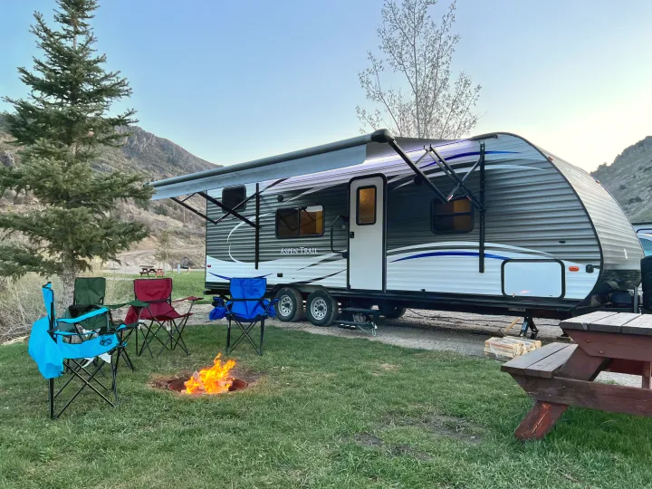 Camping bliss with an Aspen Trail RV rental, a cozy campfire, chairs, and scenic mountains at dusk.. Aspen Trail Aspen Trail Trailer 2018